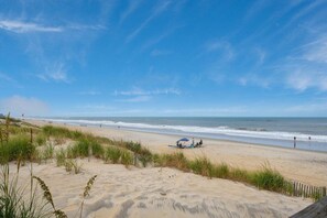 Une plage avec des dunes de sable, un ciel dégagé et l’océan.