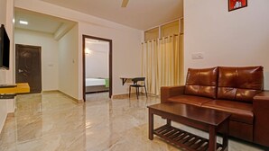 Una sala de estar con un sofá de cuero marrón, una mesa de centro de madera y una pequeña mesa con una silla. Un televisor está montado en la pared.