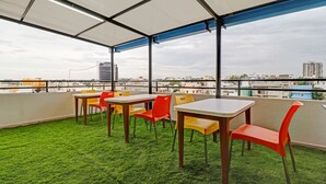 Una terraza en la azotea con piso de césped artificial verde, mesas blancas y sillas de colores.