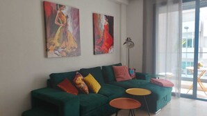 A modern living room with a green sofa, colorful cushions, two small round tables, and abstract paintings on the wall.