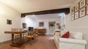 A dining area with a wooden table and chairs, a white sofa, and a staircase leading to an upper level. - Ivana Le Case di Angelina (Farigliano)