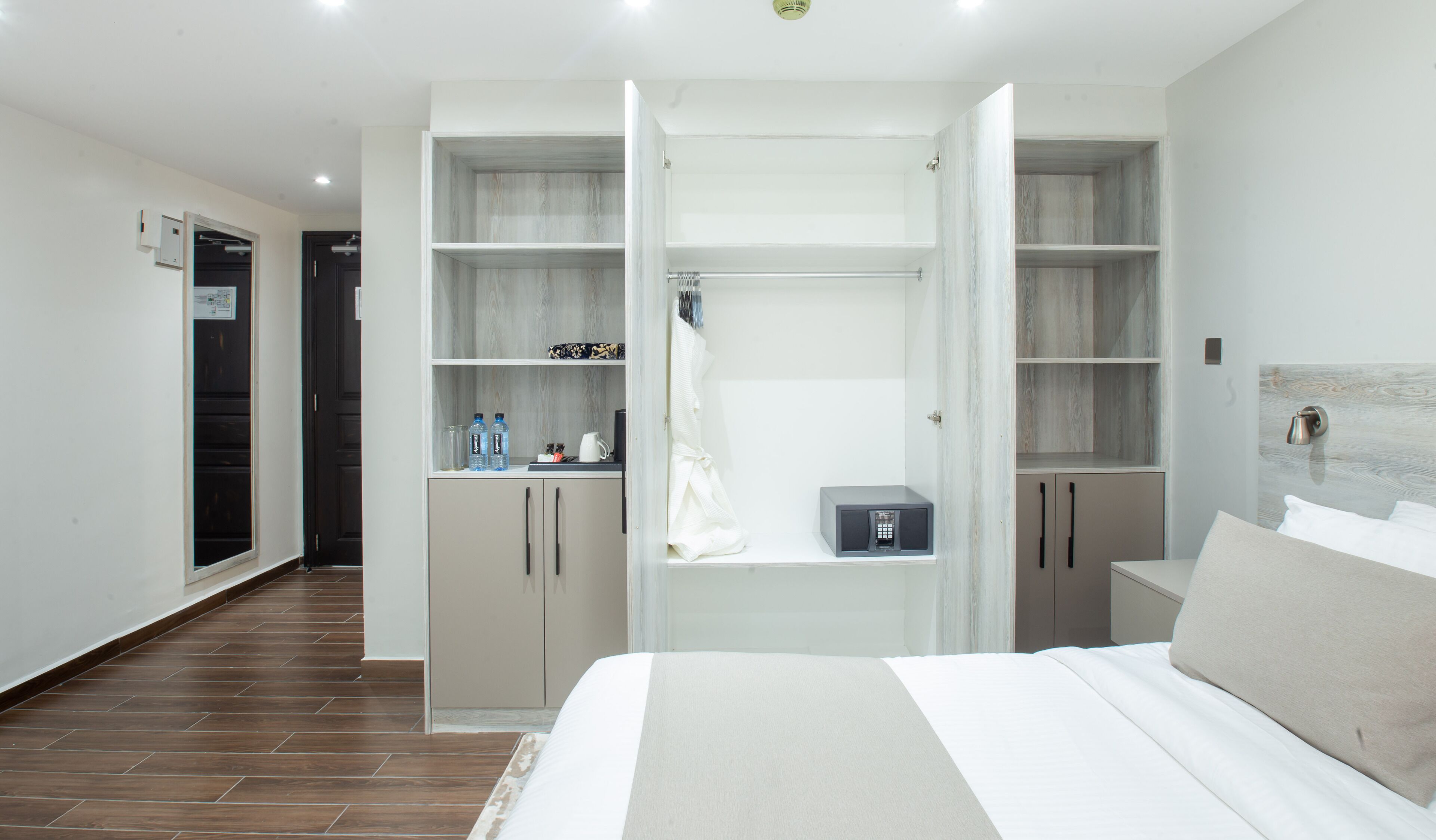 A hotel room with a large bed, a wardrobe with open doors, a small table with a kettle and bottles, and a microwave.