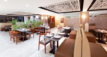 Un área de comedor moderna con varias mesas y sillas, una recepción y un espacio de descanso con un sofá.