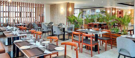 Un restaurante moderno con sillas de madera y grises, mesas dispuestas con platos, vasos y cubiertos.