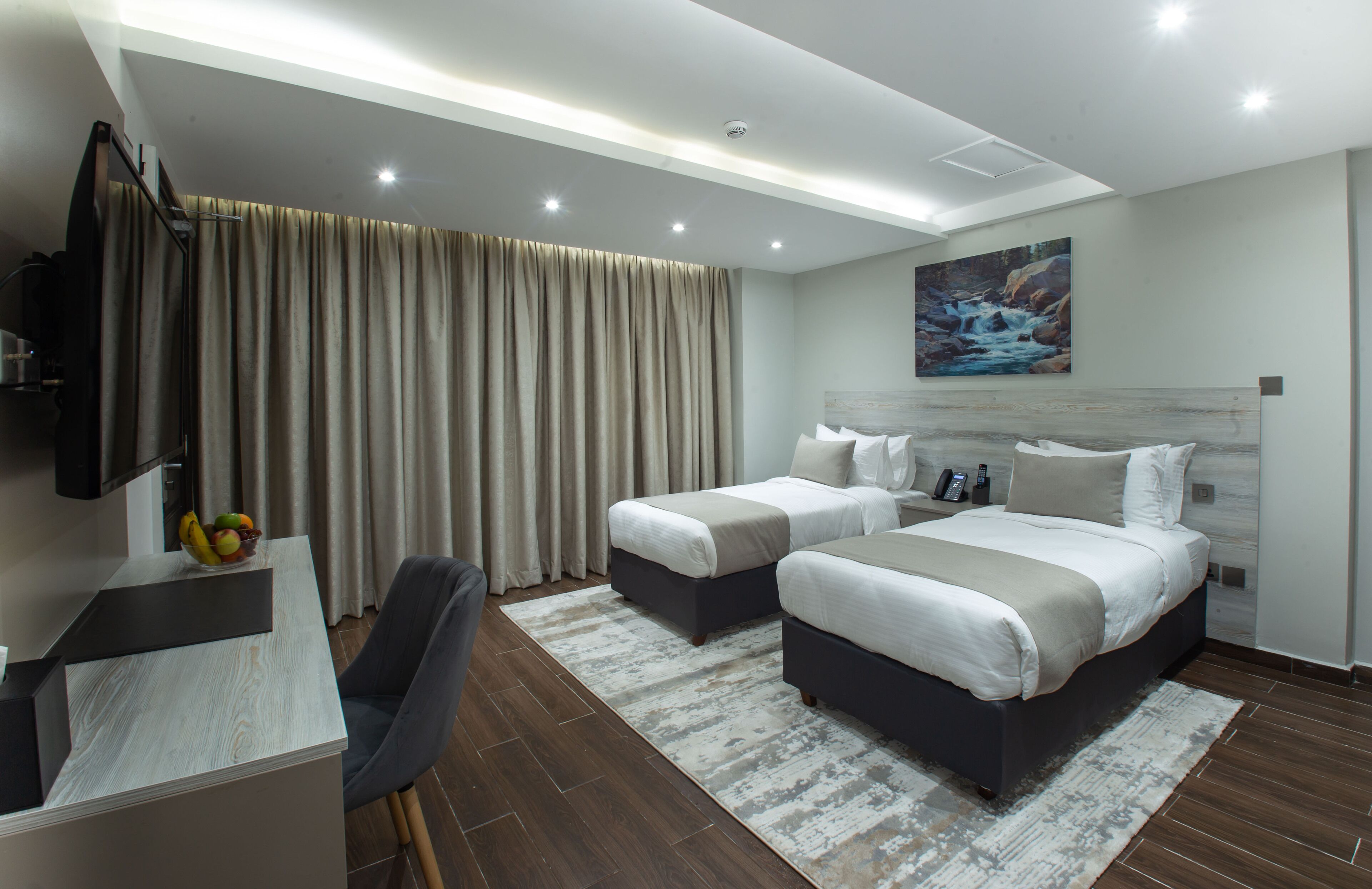 Quarto de hotel moderno com duas camas, uma escrivaninha e uma janela grande com cortinas.