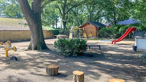 Un’area giochi con uno scivolo, altalene e un piccolo edificio in legno.