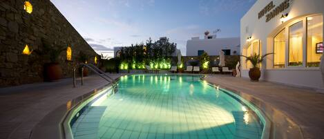 A swimming pool with a stone wall on one side and a hotel building on the other.