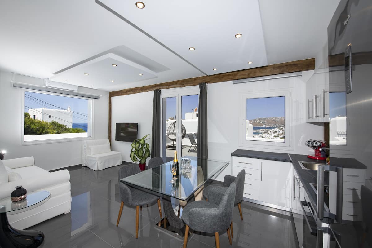 A modern kitchen with a glass dining table, grey chairs, and white cabinetry.