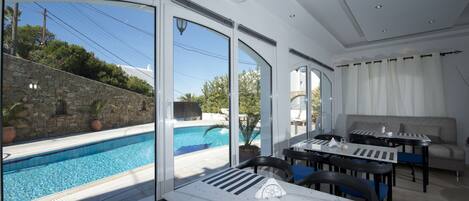 A poolside dining area with a view of the pool, stone wall, and outdoor seating.