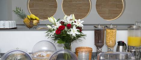 A breakfast buffet with various food items, a fruit bowl, and decorative flowers.