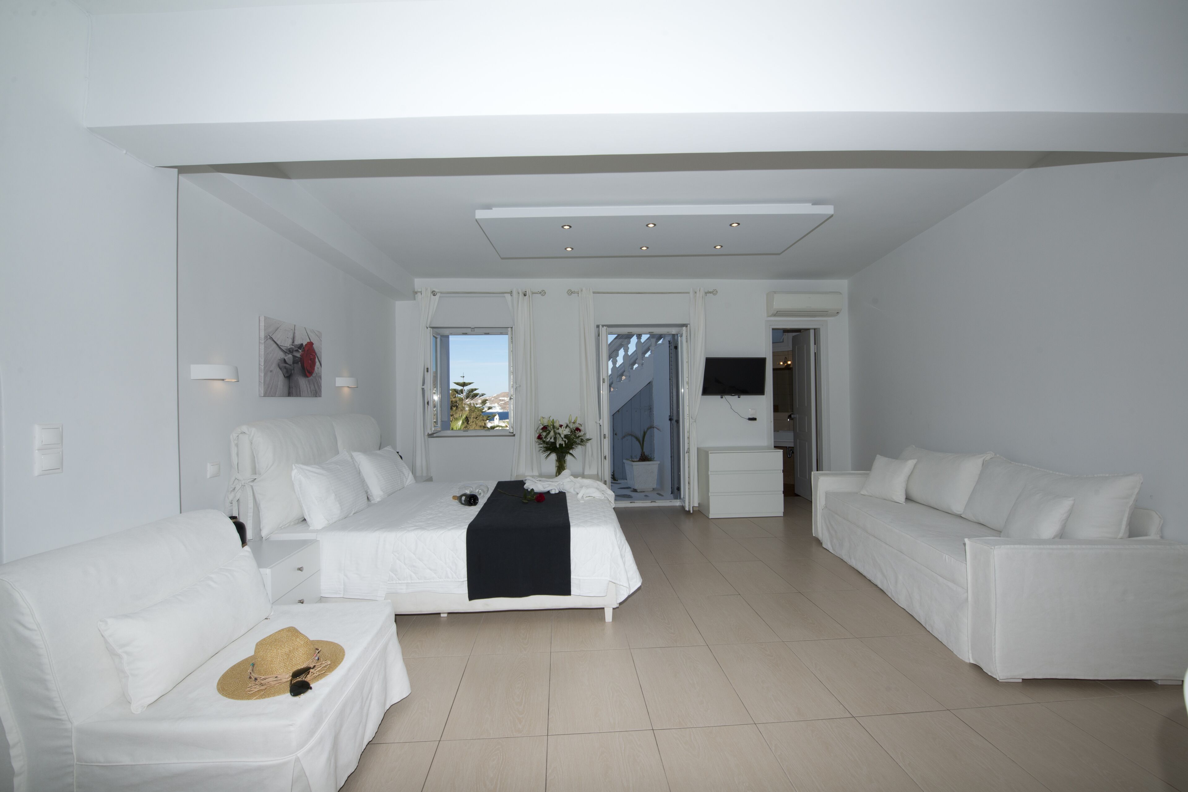 A spacious, modern hotel room with a large bed, two white sofas, and a flat-screen TV.