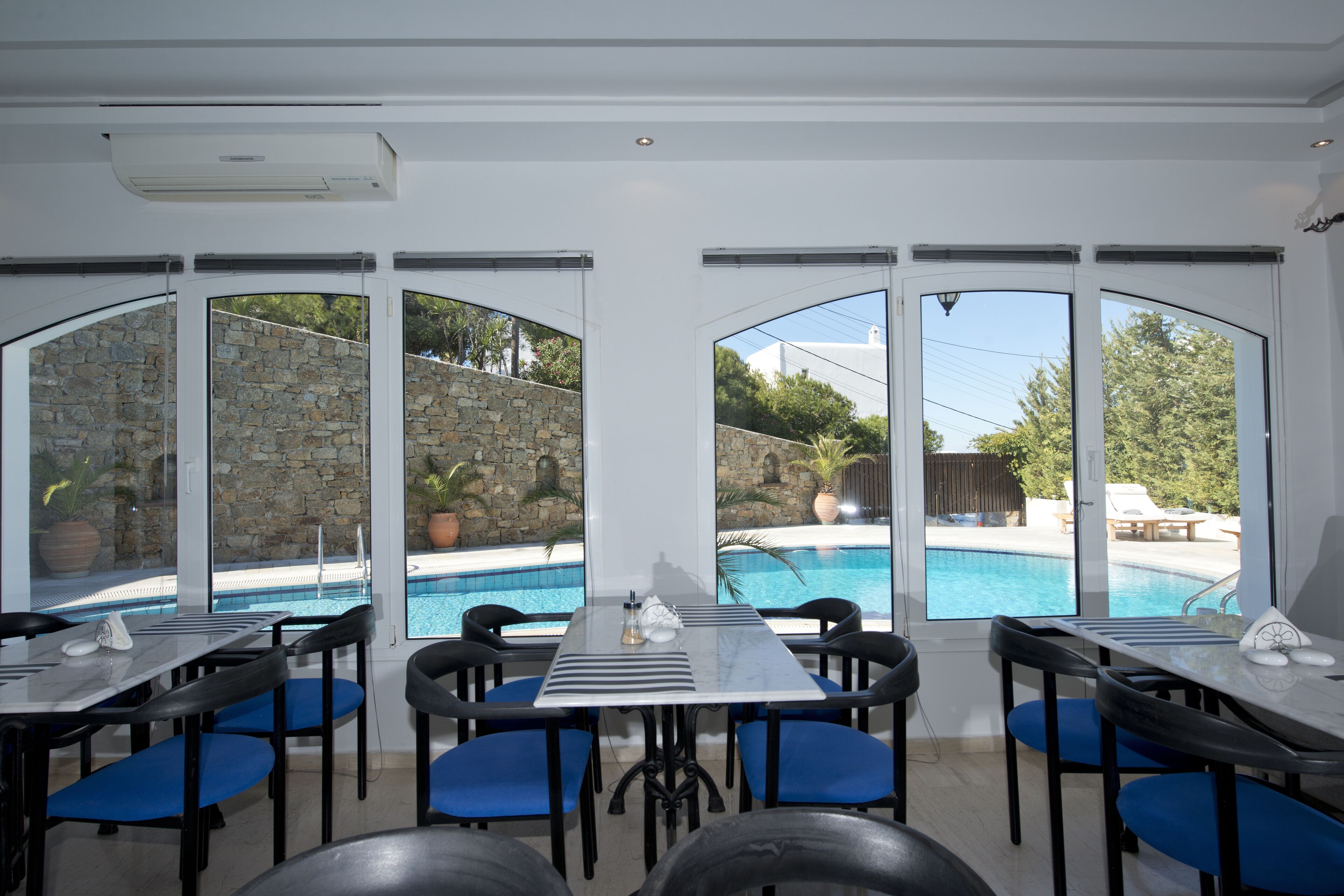 A dining area with tables and chairs, large windows, and a view of a swimming pool.