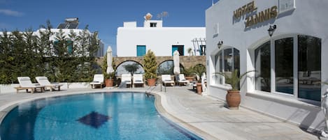 A swimming pool with lounge chairs, a stone archway, and a building labeled "Hotel Zannis".