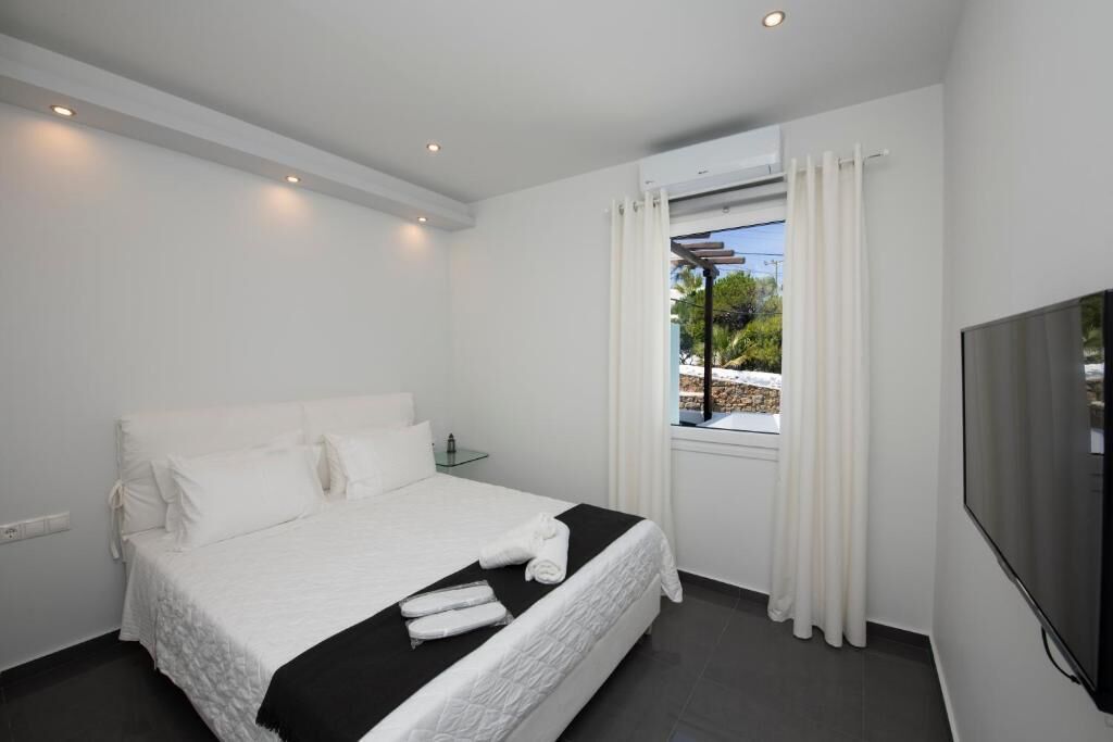 Ein Hotelzimmer mit Bett, Fernseher, Fenster mit Vorhängen und Blick ins Freie.