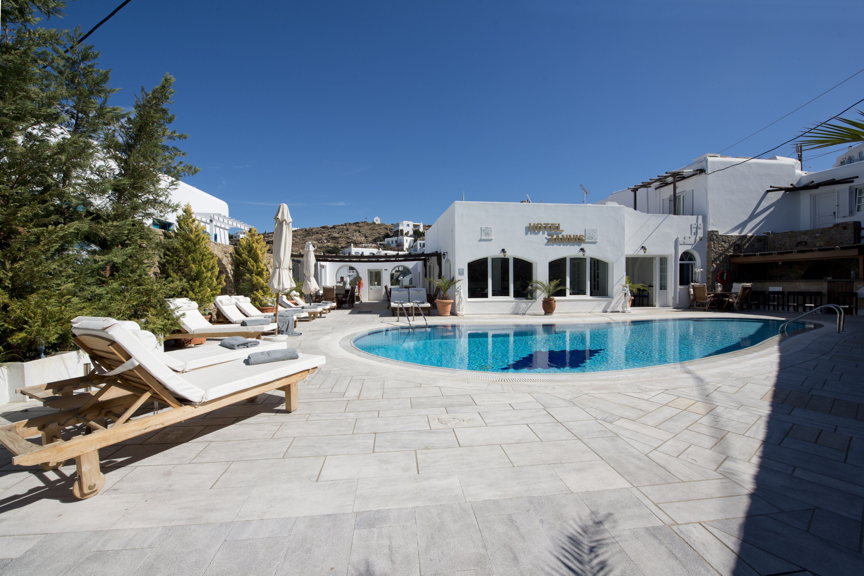 A hotel with a swimming pool, lounge chairs, and a white building with a sign.