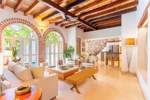 Amplia sala de estar con techo alto, vigas de madera a la vista y un gran ventanal de arco que da a una piscina.