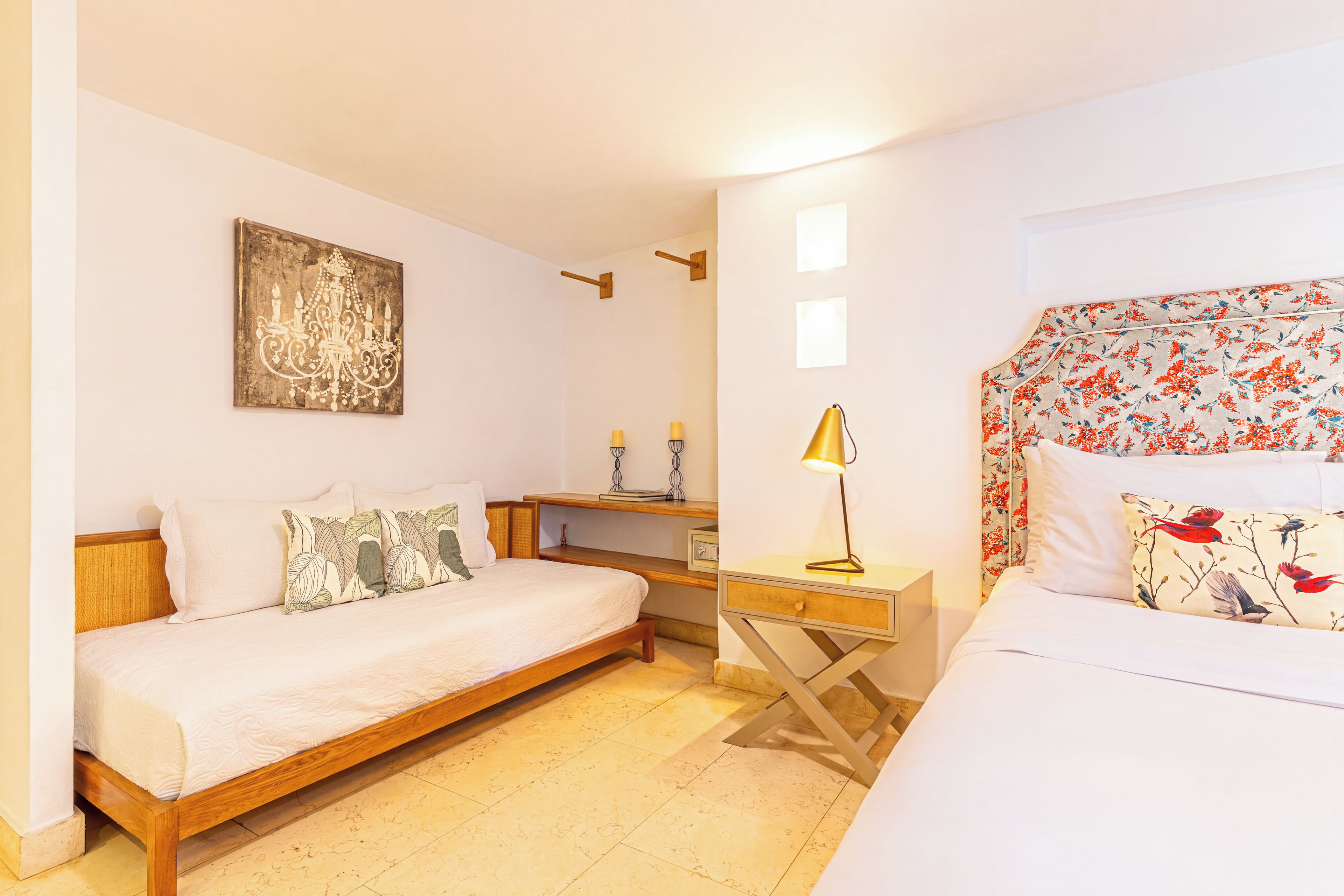 A bedroom with a wooden bed, a bedside table with a lamp, a wall-mounted artwork, and a floral-patterned headboard.