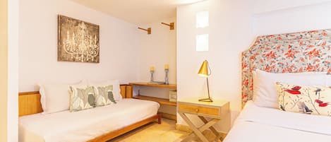 A bedroom with a wooden bed, a bedside table with a lamp, a wall-mounted artwork, and a floral-patterned headboard.