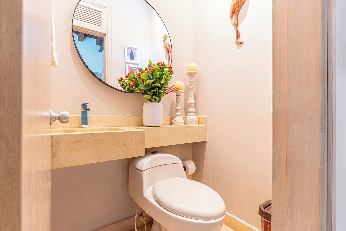 A bathroom with a toilet, a sink, a mirror, and a vase with flowers.