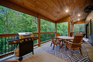 Eine überdachte Terrasse im Freien mit Grill, Holzstühlen und Tisch.