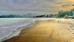Une plage avec un rivage sablonneux, des vagues douces et, en arrière-plan, des montagnes et des arbres.