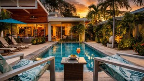 Un espace piscine avec des chaises longues, une table où l’on peut prendre un verre et manger, et une vue sur la maison.