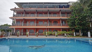 A multi-story building with a swimming pool in front. - Treebo Trend Green Palm Resorts (Neyyattinkara)