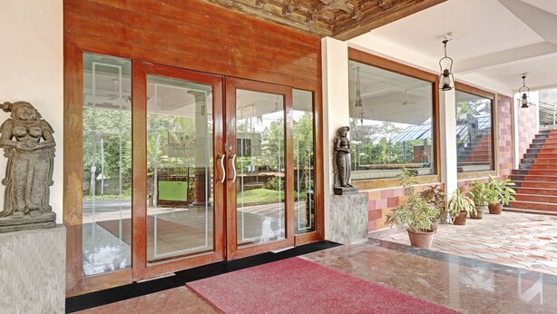 A hotel entrance with a glass door, a statue, and a staircase leading to the upper floor. - Treebo Trend Green Palm Resorts (Neyyattinkara)