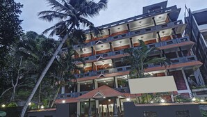 A multi-story hotel with a central entrance, balconies on each floor, and surrounding tropical vegetation. - Treebo Trend Green Palm Resorts (Neyyattinkara)