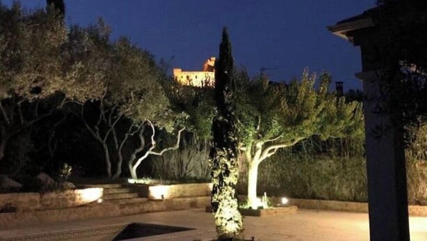 A nighttime view of a courtyard with a building in the background, surrounded by trees and illuminated by artificial lighting.