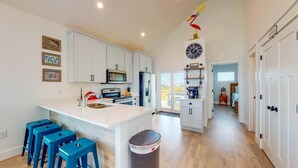 Cocina moderna con armarios blancos, una isla central con taburetes azules, un lavamanos de acero inoxidable y un cubo de basura.