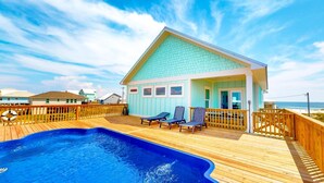 Una casa frente a la playa con piscina, terraza de madera y vista al mar.