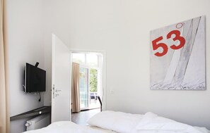 A hotel room with a bed, a TV mounted on the wall, a window with curtains, and a large number '53' artwork. - Dünenvilla Penthouse Superior (Lübeck)