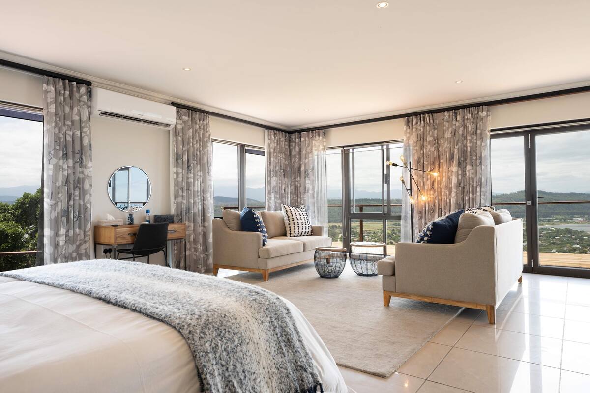 Une chambre moderne avec un grand lit, un bureau, deux canapés et une vue sur l’extérieur.