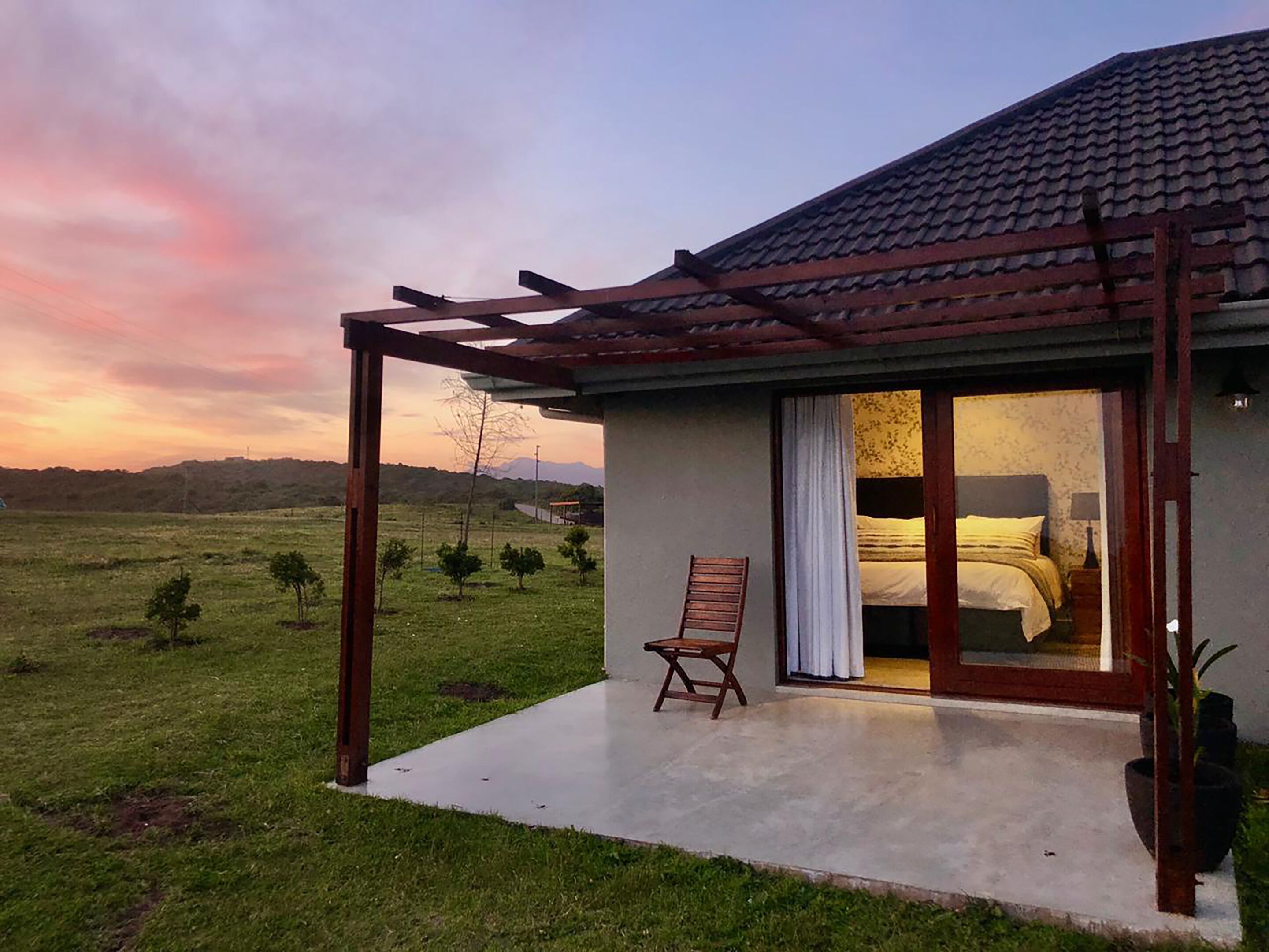 Une maison de plain-pied avec un patio, un lit visible à travers une porte vitrée et une chaise à l’extérieur.