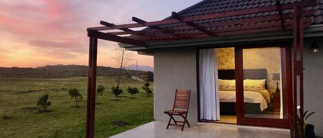 Einbungalow mit Terrasse, einem Bett, das durch eine Glastür sichtbar ist, und einem Stuhl draußen.
