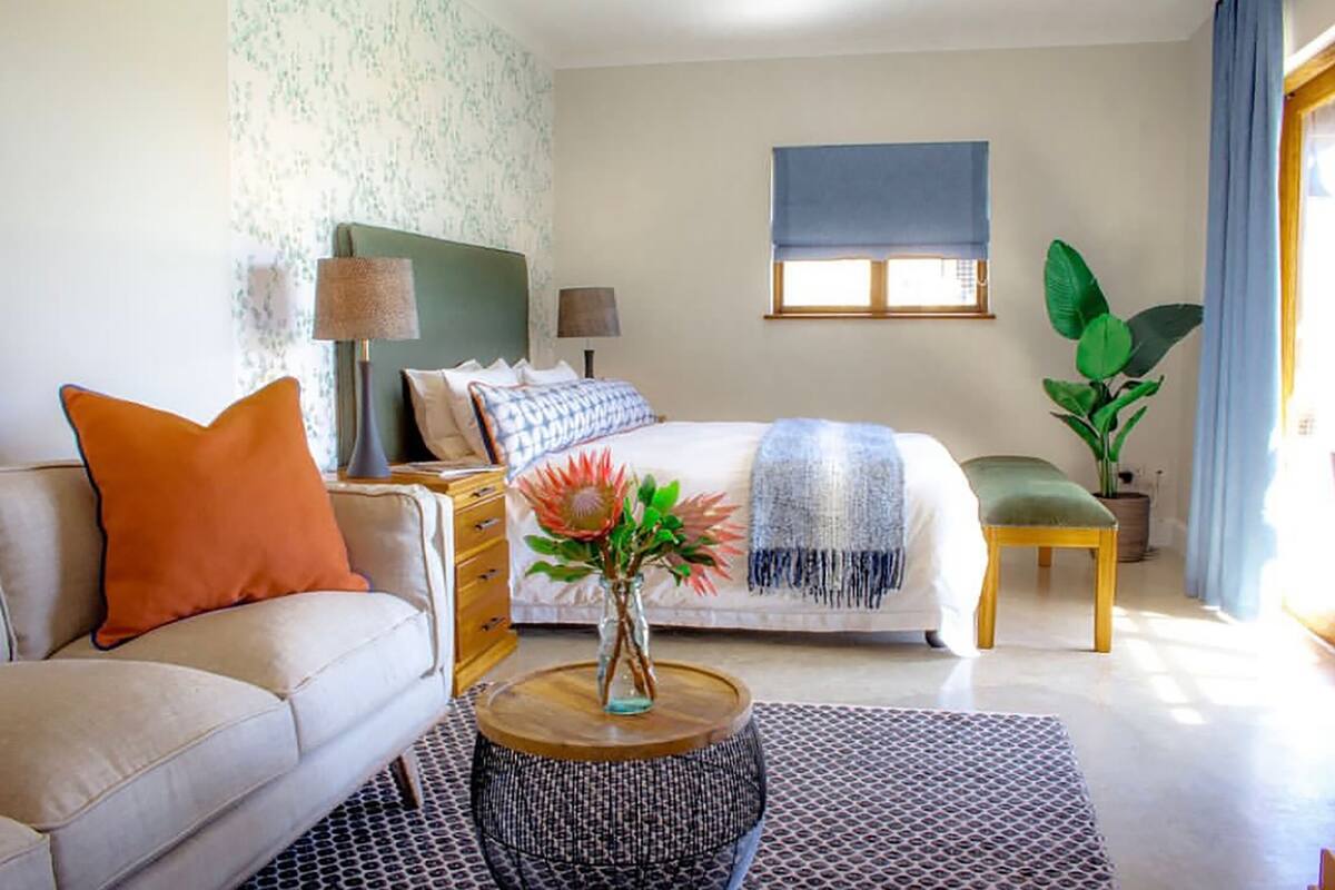 Une chambre à coucher avec un lit, un canapé, une table basse, une lampe, une plante et une fenêtre.