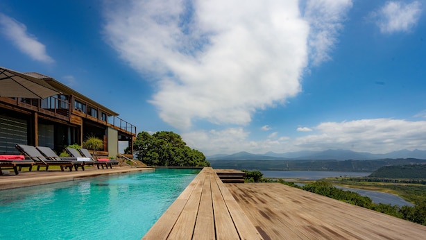 Une terrasse en bois mène à une piscine équipée de chaises longues, un espace abrité et offre une vue sur les montagnes et un lac.
