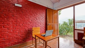 Una habitación con pared de ladrillo rojo, una puerta de madera y un ordenador portátil sobre una mesa de madera.