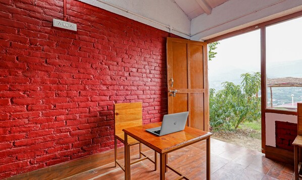 A room with a red brick wall, a wooden door, and a laptop on a wooden table. - Treebo Om Villa With Mountain View (Dhari)