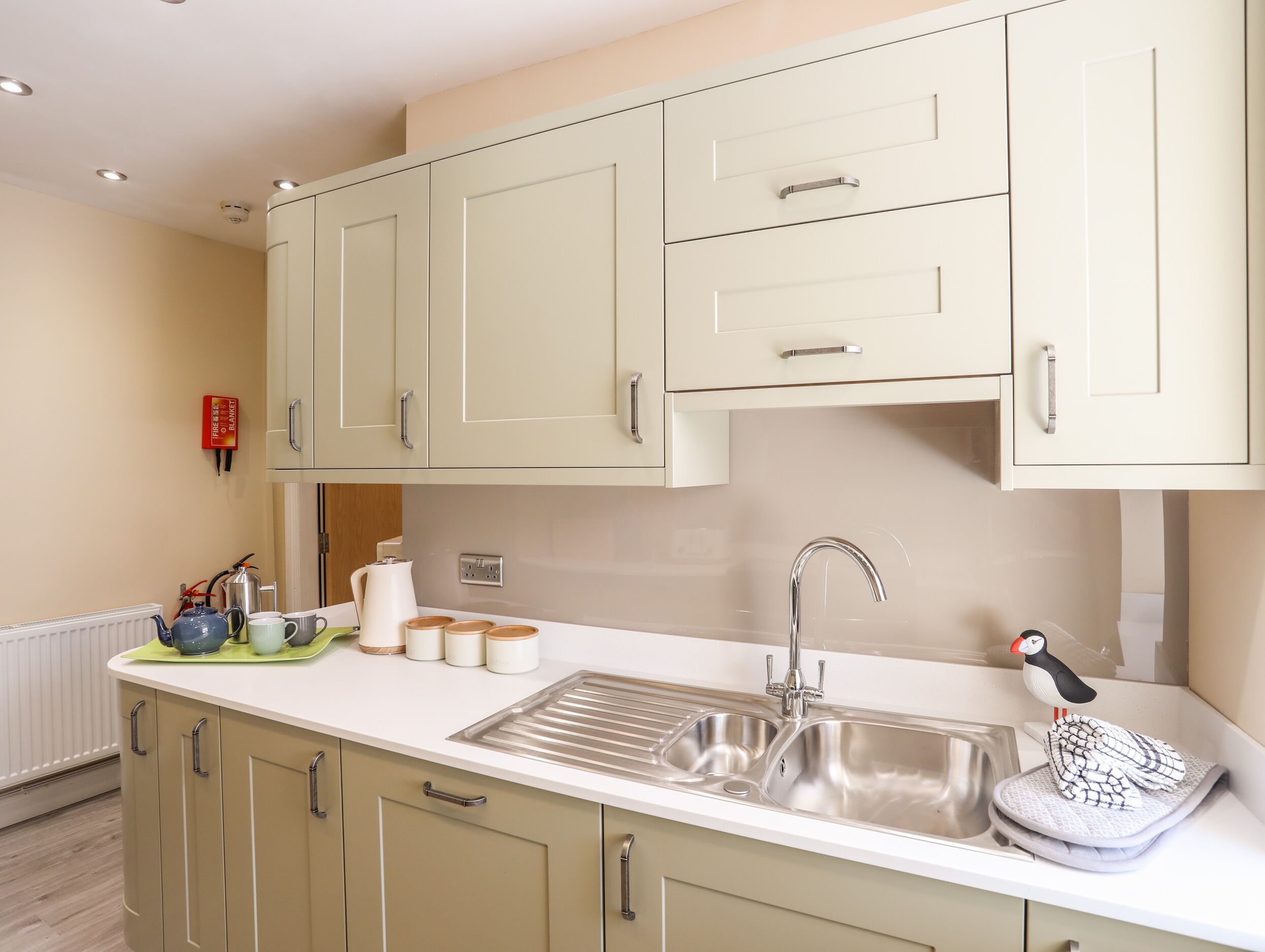 A kitchen with light-colored cabinets, a double sink, and a kettle on the counter.