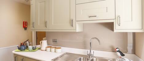 A kitchen with light-colored cabinets, a double sink, and a kettle on the counter.