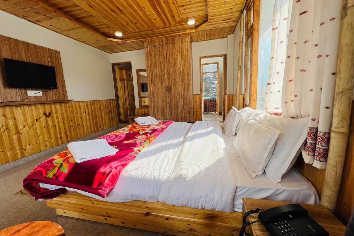 Una habitación con paneles de madera, una cama, un televisor montado en la pared y una mesita de noche de madera con un teléfono.