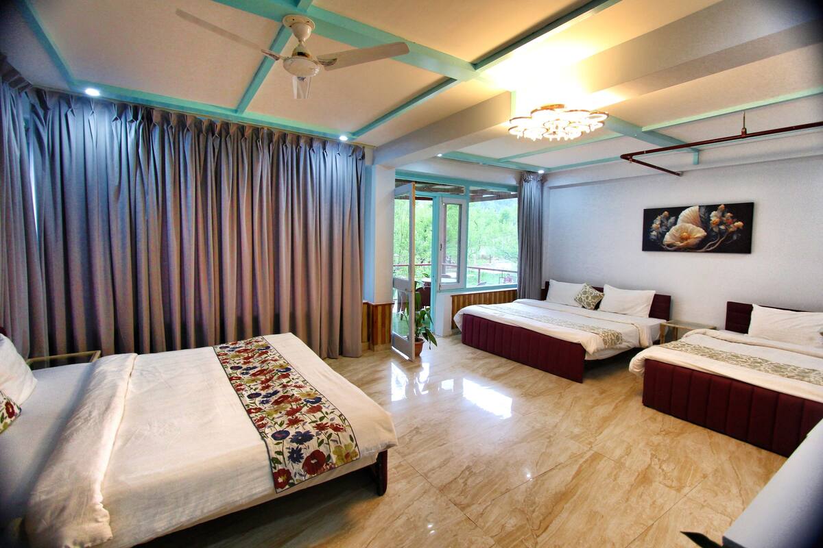 Habitación de hotel con dos camas, ventilador de techo, candelabro y un ventanal con cortinas.