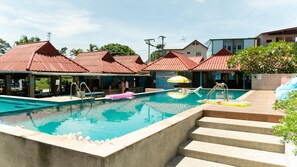 Piscina con escalones de acceso, rodeada de zonas de estar cubiertas con techos rojos.
