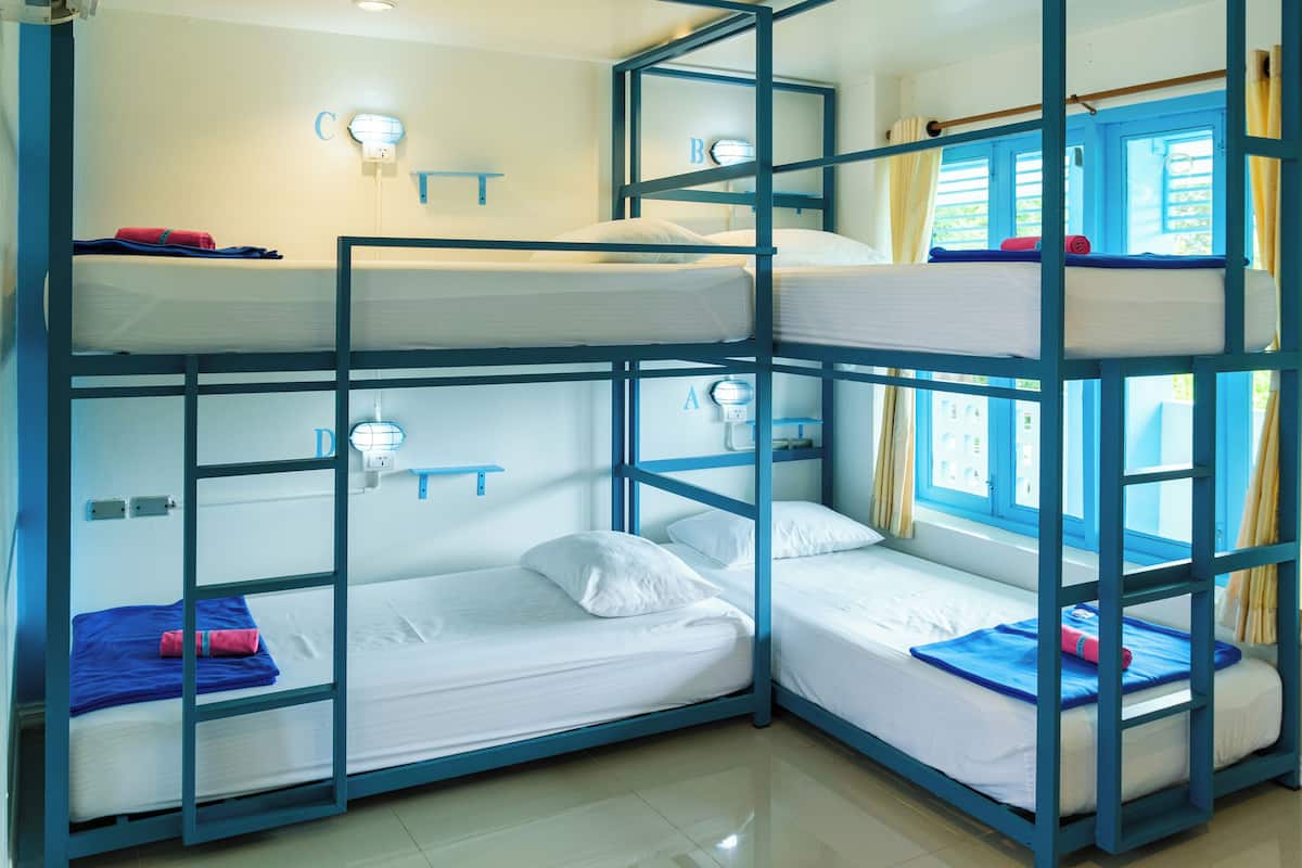 A bunk bed room with three levels, each with a pillow and a blanket. There are wall-mounted lights above each bed.