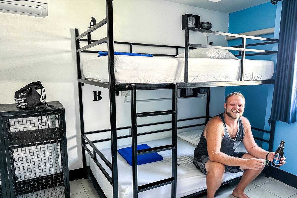 A bunk bed room with a black metal frame, a blue pillow on the lower bunk, and a black bag on a shelf.