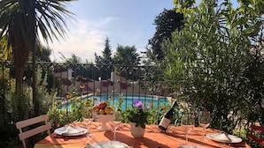 Un área de comedor al aire libre con una mesa preparada para dos personas, rodeada de abundante vegetación y vistas a una piscina.