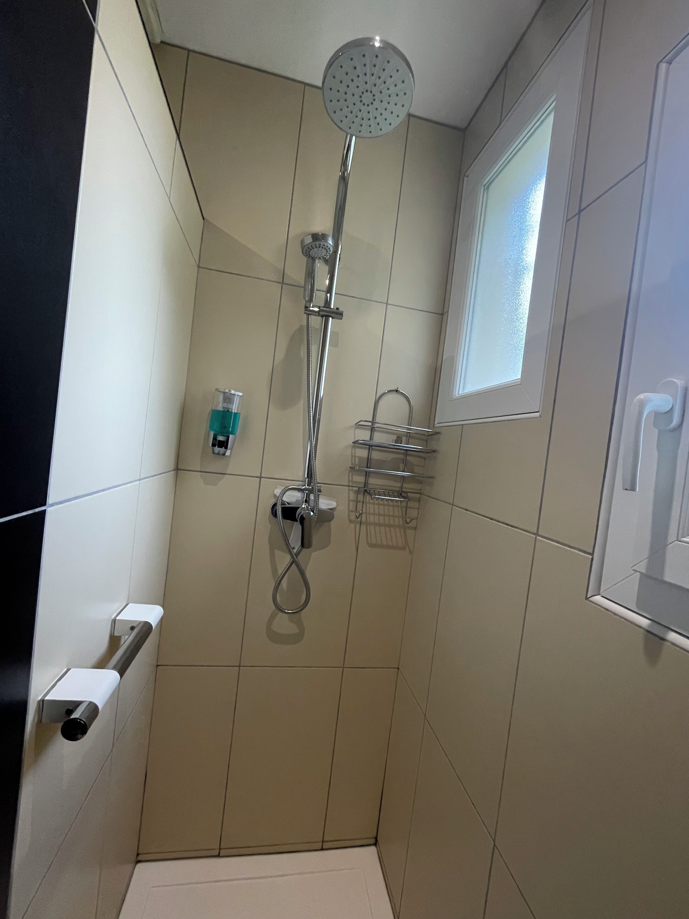 A small, tiled bathroom with a shower, a window, and a towel rack.