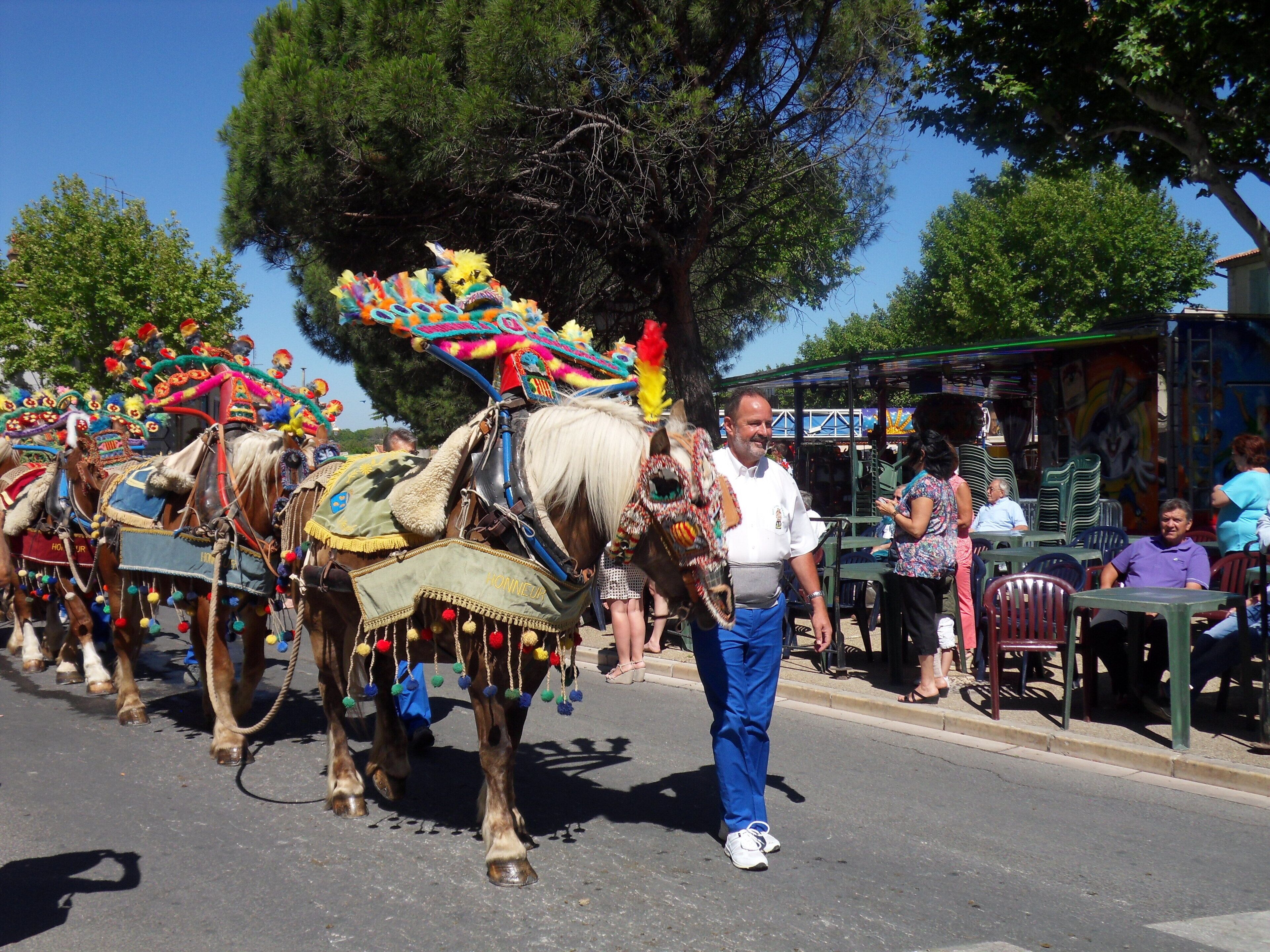 A street parade with decorated horses and riders, a crowd of onlookers, and outdoor seating areas.